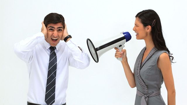 Video shows a woman in formal attire shouting into a megaphone at a businessman covering his ears out of frustration. Suitable for illustrating themes like workplace stress, communication issues, conflict resolution, or teamwork dynamics.