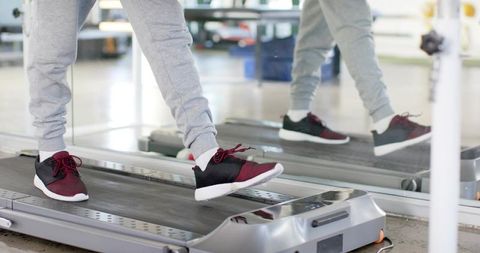 Male walking on treadmill wearing maroon sneakers and grey joggers with mirror reflection