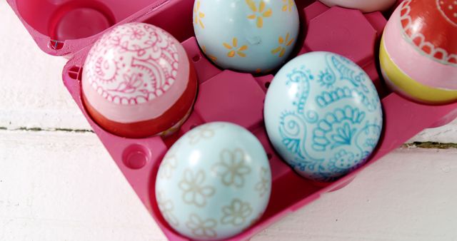 Colorful painted eggs rest in a pink egg carton, symbolizing Easter traditions. Their intricate designs reflect the festive spirit and creativity associated with the holiday.