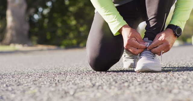 Person tying shoes on road, preparing for a run. Ideal for fitness advertisements, exercise blogs, sportswear promotions.