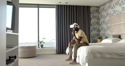 Man sitting on bed enjoying virtual reality in modern bedroom