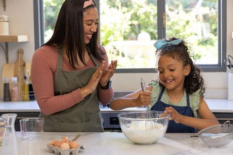 Mother daughter whisking batter together in bright sunlit kitchen