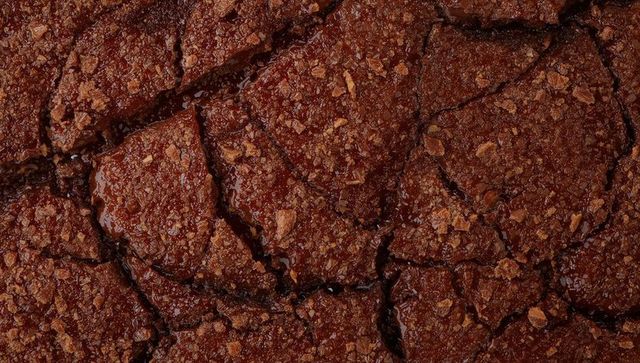 Closeup showing cracked fudgy chocolate brownie crust with glossy pockets and crumb texture