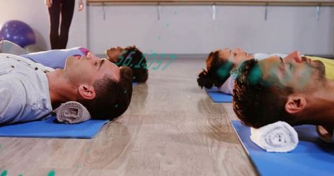 Group cooling down after workout, adults lying on mats with towels under necks