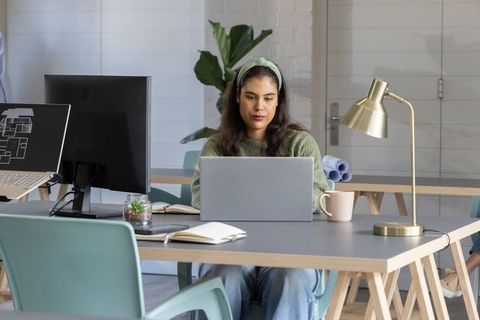 Young architect working on laptop at modern coworking table with floor plan monitor
