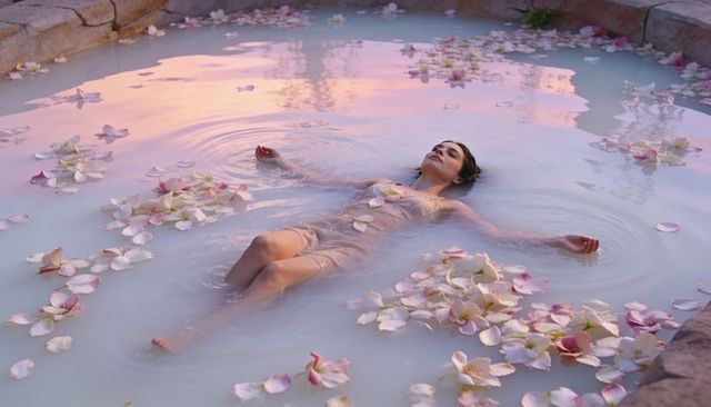 Woman floating in milky flower-filled pool at pastel sunset