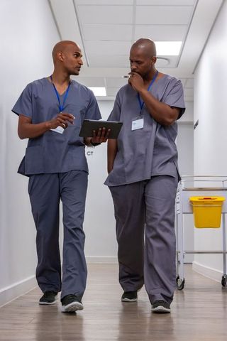 African american medics walking hospital corridor reviewing tablet for teamwork