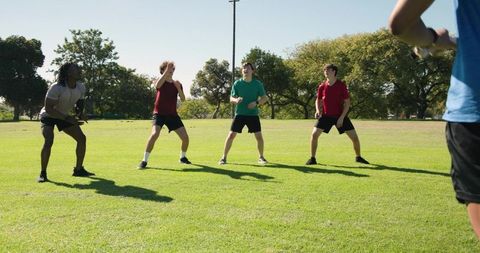 Youth athletes practicing catching drill with coach on sunny grass field