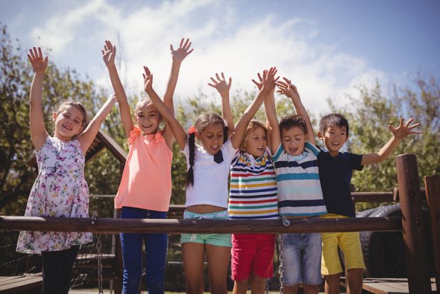 Group of cheerful children raising their hands while playing in a school playground. Ideal for use in educational materials, advertisements for children's products, or articles about childhood development and outdoor activities.