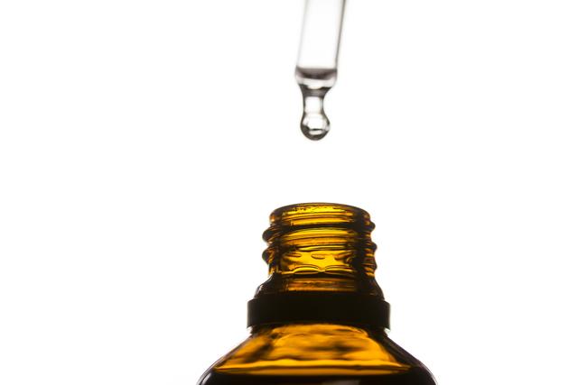 This image captures a close-up view of a drop of essential oil dripping from a pipette into a bottle. It is ideal for use in articles or advertisements related to aromatherapy, wellness, skincare, and natural health products. The image can also be used in blogs or social media posts promoting holistic and alternative medicine practices.