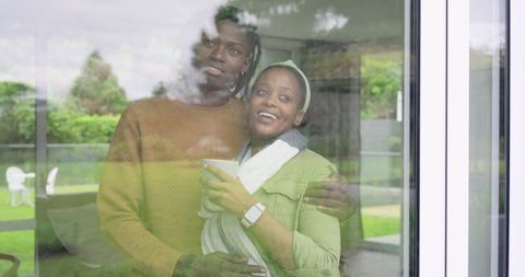 African American couple standing behind glass door embracing, smiling, holding warm mug