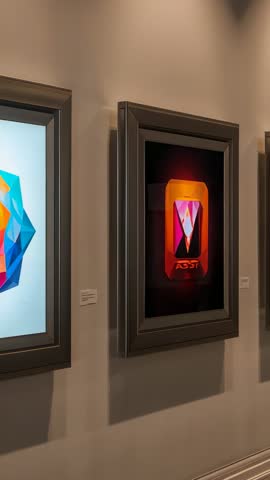 Vertical video panning gallery wall displaying framed geometric digital art in spotlights