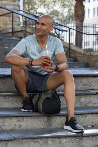 African american athlete resting on urban steps holding cold drink and duffel bag, smiling