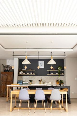 Modern minimalist open-concept kitchen featuring long wooden dining table and four gray chairs