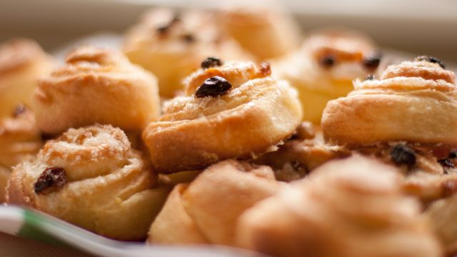 This image depicts a close-up view of freshly baked cinnamon rolls adorned with raisins. The golden-brown pastries exude a warm and inviting appearance, making them suitable for use in food blogs, bakery advertisements, recipe books, and any culinary website. Perfect for visuals that aim to convey warmth, home-cooked comfort, and delicious bakery items.