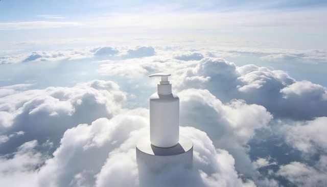 Matte white pump bottle on pedestal floating above clouds conveying pure skincare