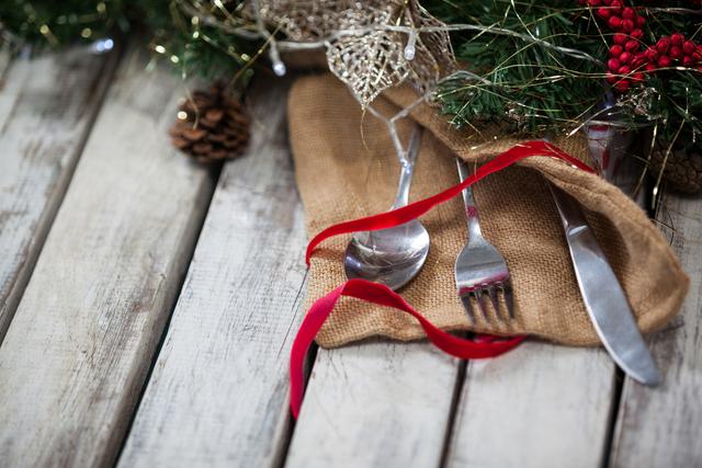 Perfect for holiday-themed content, this image showcases a rustic Christmas table setting with cutlery wrapped in burlap and adorned with a red ribbon. Ideal for use in festive dining promotions, holiday recipes, or seasonal blog posts.