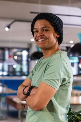 Young african american man smiling in coworking space wearing beanie and bracelets