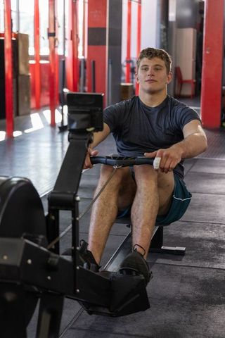 Young athlete rowing on ergometer in gym pulling handle for cardio strength training