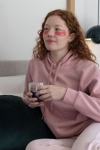 Evening self care ritual wearing pink under-eye gel patches holding dark red drink