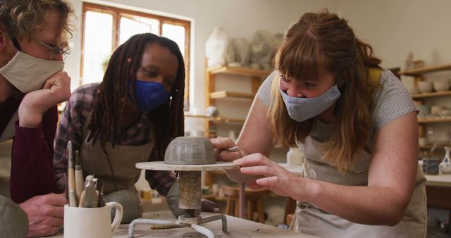 Diverse potters wearing face masks and aprons working on pot on potters wheel at pottery studio. hygiene and social distancing in the pottery studio during coronavirus covid 19 pandemic