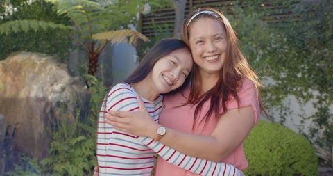 Asian mother and daughter hugging outdoors with affection