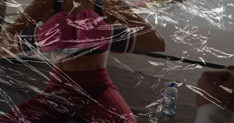 Adjusting female boxer in pink training set holding gloves amid boxing ring ropes with wrap glare