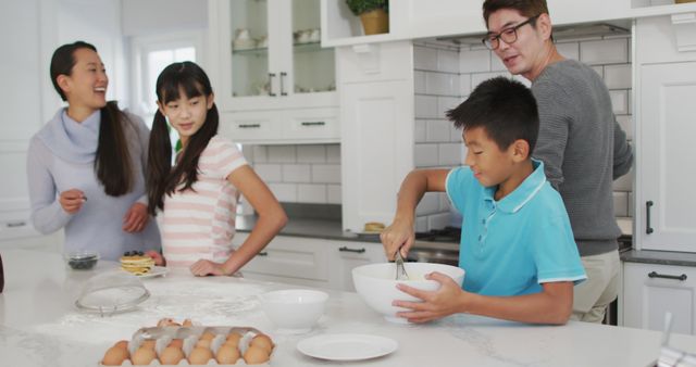 Asian family, including parents and children, participating in baking activities in a bright, modern kitchen. This image can be used for promoting family activities, cooking tutorials, educational materials on family bonding, and advertisements targeting family products or kitchenware.