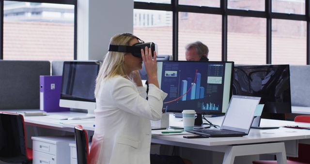 A businesswoman sits at her office desk intently using a VR headset, showcasing a modern and technology-driven workspace. This can be used for themes of innovation, professional development, and the integration of virtual reality in business settings. Ideal for articles and digital content discussing futuristic workplaces, technology in business, or showcasing diversity and inclusivity in a corporate environment.