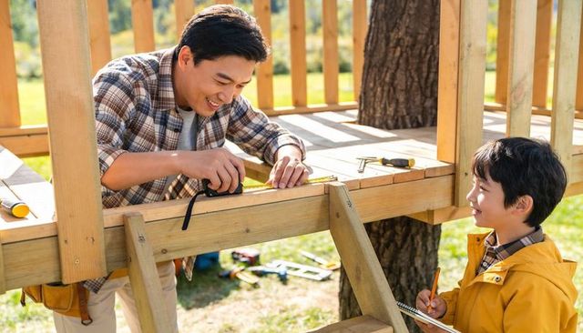 Father and son building backyard treehouse measuring and marking wood with tape measure