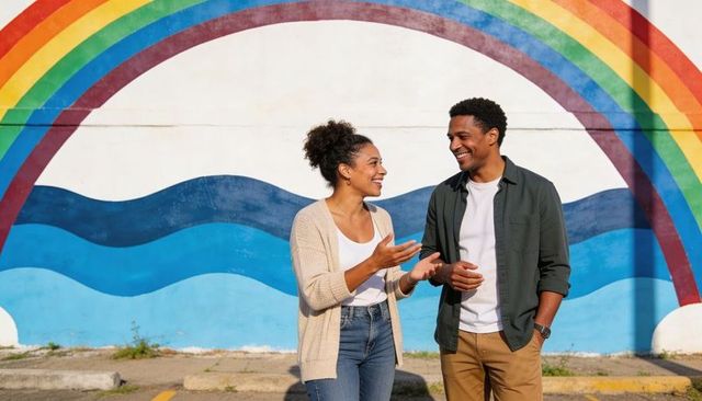 Smiling couple chatting in front of rainbow mural urban lifestyle conversation outdoors