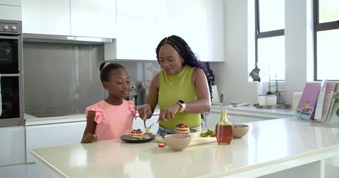 Mother and daughter preparing pancakes at bright modern kitchen island