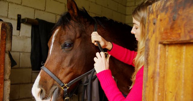 This image shows a young woman grooming a horse in a stable. Ideal for use in themes related to animal care, equestrian activities, countryside lifestyle, and rural settings. Perfect for blogs, articles, or promotions focusing on horse riding, pet care, or outdoor activities.