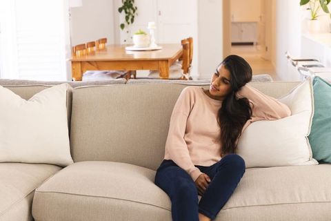 Relaxed south asian woman sitting on comfortable sofa in bright living room