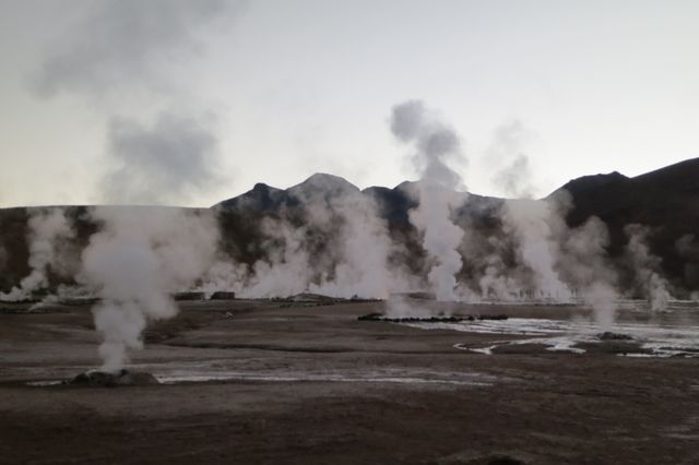 Geysers emitting steam in a rugged mountain landscape during dusk. Ideal for use in travel articles, educational materials about geothermal activity, or promotional content for adventure tourism. Featuring an arid terrain that highlights the raw power and beauty of natural phenomena.