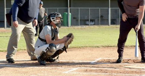 Baseball catcher squatting behind home plate with umpire and batter preparing to swing
