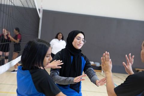 Teen athletes wearing hijab and jerseys giving high-fives on indoor volleyball court