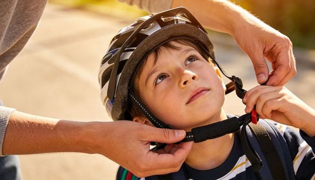 Parent fastening bike helmet strap on young boy preparing for outdoor ride