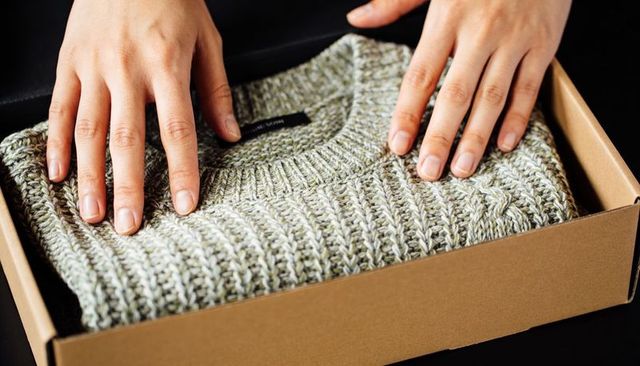 Hands smoothing folded knit sweater in eco packaging box for online retail