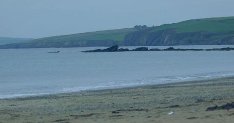 Sandy beach with pebbles and seaweed, lapping waves and rocky outcrops by green cliffs