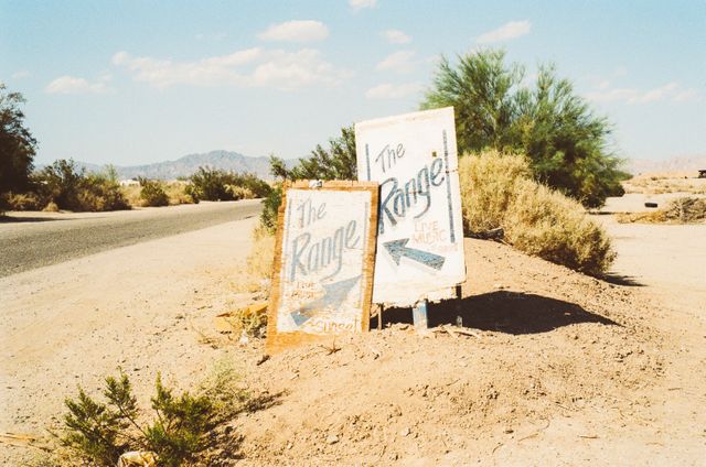 This image features two vintage signs for 'The Range' on a remote desert road, with an arid landscape and sparse vegetation in the background. The image evokes a sense of adventure and nostalgia, making it perfect for use in travel blogs, tourism advertisements, retro-themed projects, and wilderness exploration content.