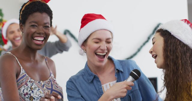 Happy group of diverse friends singing karaoke at christmas party. Spending quality time at home together at christmas.