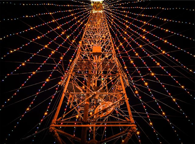 Mesmerizing shot depicting a Ferris wheel at night with radiating, colorful lights. Useful for articles, blogs, or advertisements related to carnivals, festivals, nightlife entertainment, amusement parks, or vibrant cityscapes. Perfect for showcasing the joy of night-time festivities and eye-catching attractions.