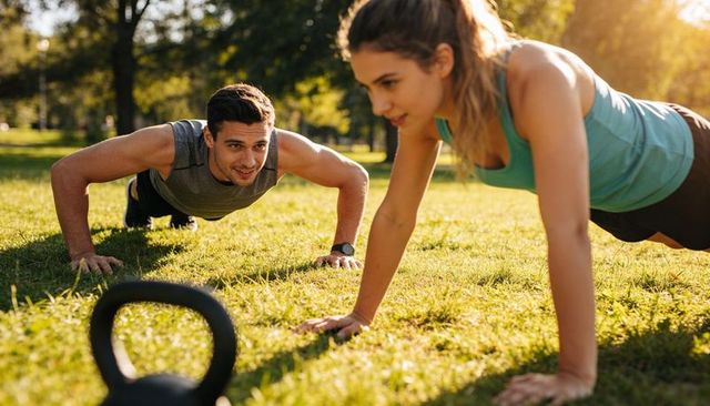 Couple performing push-ups in park during golden hour with kettlebell for outdoor fitness