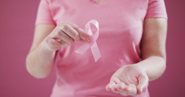 Mid section of woman holding a pink ribbon against pink background. breast cancer awareness concept