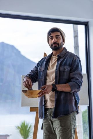 Artist mixing paint in wooden bowl at easel in lake-view studio with mountain backdrop
