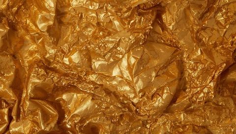 Shimmering crumpled gold foil texture reflecting light, wrinkled metallic surface macro