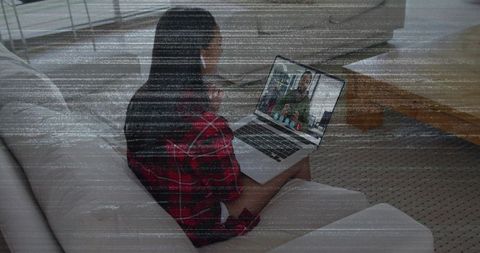 Woman sitting on sofa wearing red plaid shirt using laptop for remote work