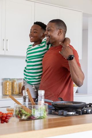 African american father carrying son at kitchen island cooking and laughing