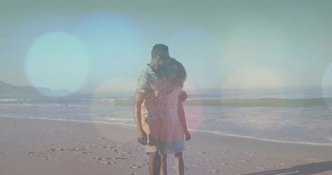 Couple walking on beach at sunset with warm lens flare, footprints and ocean bokeh